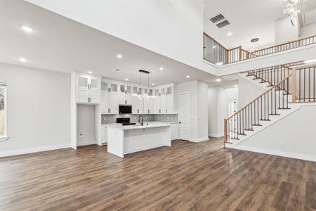 Kitchen with white cabinets, decorative light fixtures, black / electric stove, dark hardwood / wood-style flooring, and a center island with sink