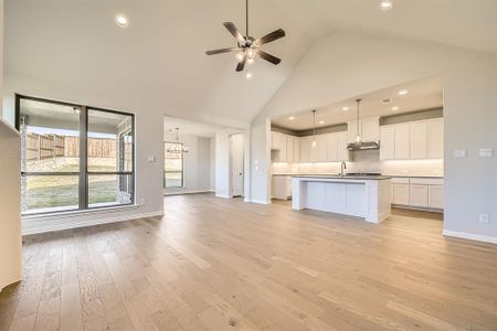 Kitchen with high vaulted ceiling, light hardwood / wood-style floors, a center island with sink, white cabinets, and ceiling fan with notable chandelier