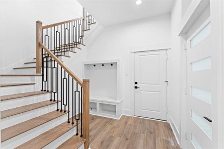 This photo showcases a modern, bright entryway featuring a wooden staircase with sleek black metal railings. The space has light wood flooring, a white door, and a built-in nook with storage and hooks, offering functionality and style.