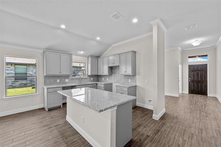 Kitchen featuring lofted ceiling, a kitchen island, hardwood / wood-style floors, gray cabinets, and light stone counters