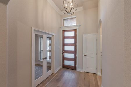 Entrance foyer featuring french doors, ornamental molding, a high ceiling, a notable chandelier, and hardwood / wood-style floors