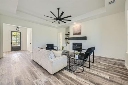 Living room featuring ceiling fan, a tray ceiling, a brick fireplace, and hardwood / wood-style floors