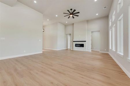 Unfurnished living room featuring ceiling fan, a high ceiling, and light hardwood / wood-style flooring