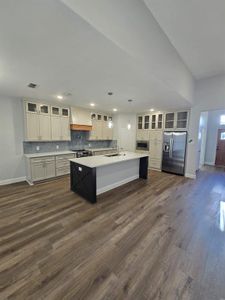 Kitchen featuring premium range hood, dark hardwood / wood-style flooring, hanging light fixtures, appliances with stainless steel finishes, and a center island with sink