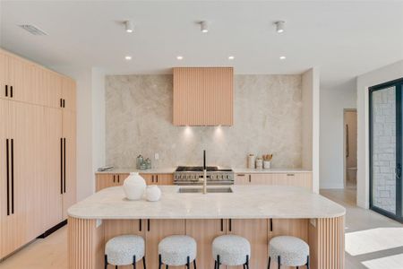 Kitchen featuring a breakfast bar area, wall chimney exhaust hood, a center island with sink, and decorative backsplash