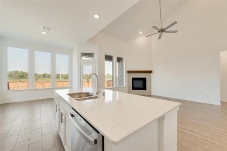 Kitchen featuring a tile fireplace, white cabinetry, dishwasher, sink, and an island with sink