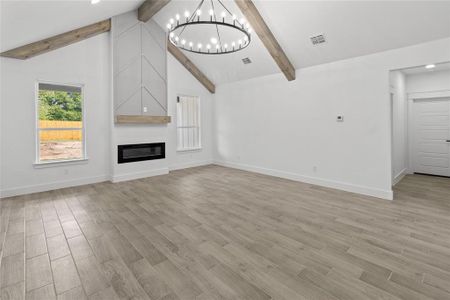 Unfurnished living room with a fireplace, light hardwood / wood-style flooring, a notable chandelier, beam ceiling, and high vaulted ceiling