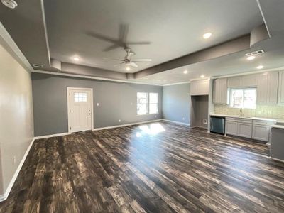 Unfurnished living room featuring ceiling fan, sink, a tray ceiling, and dark hardwood / wood-style flooring