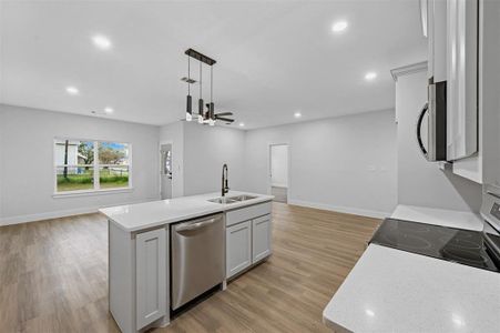 Kitchen with stove, stainless steel dishwasher, sink, a center island with sink, and white cabinetry