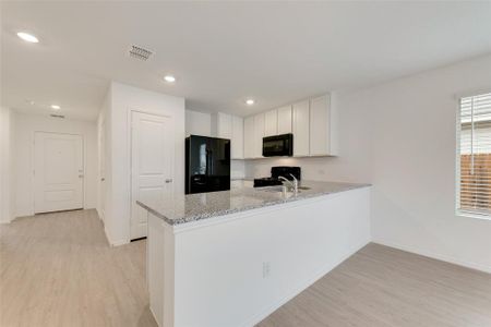 Kitchen featuring white cabinetry, light stone counters, light hardwood / wood-style floors, black appliances, and kitchen peninsula