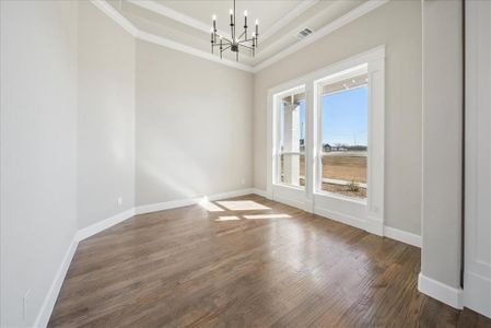 Spare room with crown molding, a notable chandelier, a tray ceiling, and dark wood-type flooring