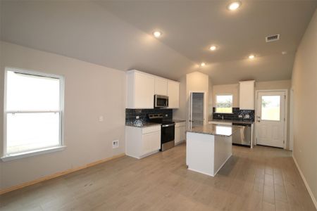 Kitchen with white cabinetry, stainless steel appliances, dark stone counters, vaulted ceiling, and a kitchen island