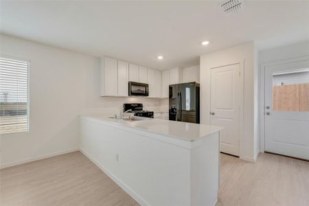 Kitchen featuring white cabinetry, light hardwood / wood-style flooring, kitchen peninsula, and black appliances