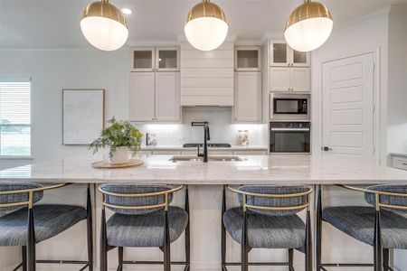 Kitchen featuring custom cabinetry to the ceiling, light hardwood floors, large island with Quartzite countertops, and beautiful hardware.