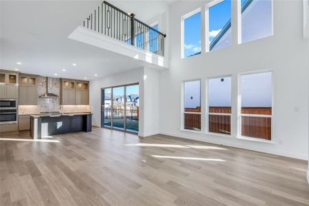 Unfurnished living room with a towering ceiling, sink, and light wood-type flooring