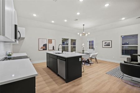 Kitchen with pendant lighting, a center island with sink, white cabinets, light hardwood / wood-style flooring, and appliances with stainless steel finishes