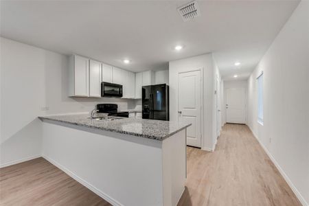 Kitchen with white cabinets, light wood-type flooring, black appliances, and light stone counters