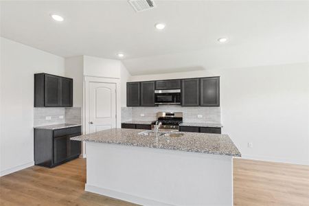 Kitchen with a center island with sink, light stone counters, stainless steel appliances, and light hardwood / wood-style flooring