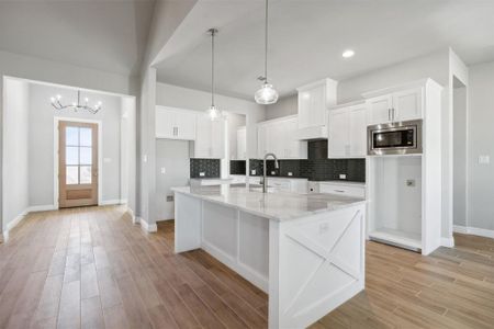 Kitchen with tasteful backsplash, white cabinets, pendant lighting, stainless steel microwave, and an island with sink