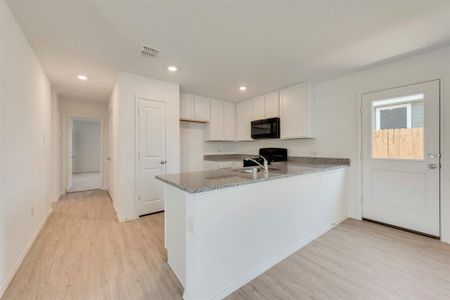 Kitchen featuring light hardwood / wood-style flooring, white cabinetry, light stone countertops, stove, and kitchen peninsula