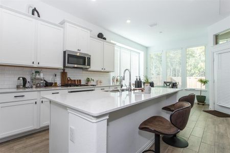 Kitchen featuring light stone counters, white cabinetry, and an island with sink