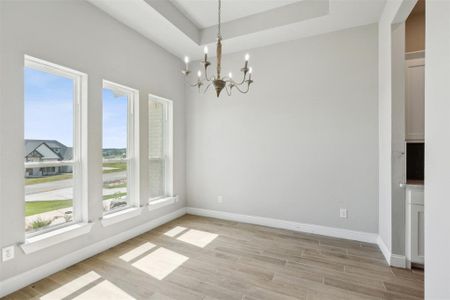 Unfurnished dining area with light wood-type flooring, a raised ceiling, and a notable chandelier