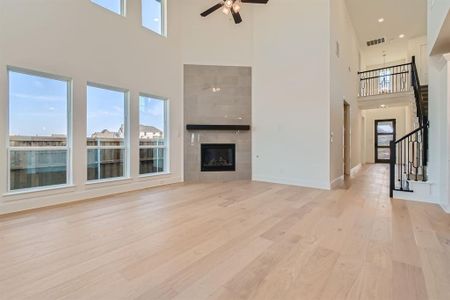 Unfurnished living room featuring a tiled fireplace, a towering ceiling, light wood-type flooring, and ceiling fan