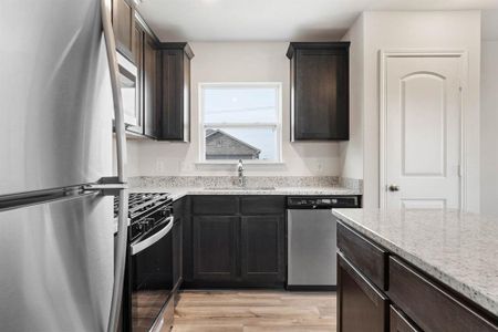 Kitchen with light wood-type flooring, stainless steel appliances, light stone countertops, dark brown cabinetry, and sink