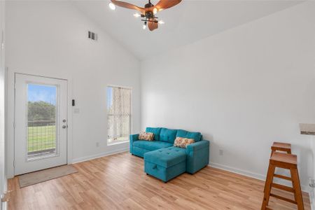 This is a bright, open-concept living room with vaulted ceilings,  and plenty of natural light. The room includes a modern ceiling fan providing a comfortable and airy space for relaxation.