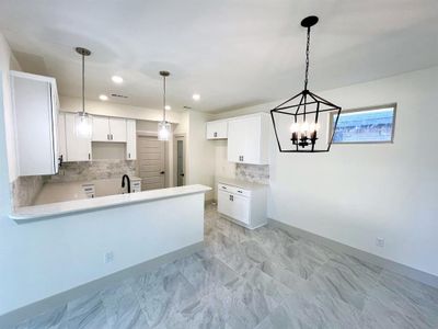 Kitchen with pendant lighting, sink, kitchen peninsula, white cabinetry, and an inviting chandelier