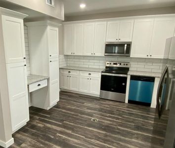 Kitchen with white cabinets, appliances with stainless steel finishes, dark hardwood / wood-style floors, and decorative backsplash