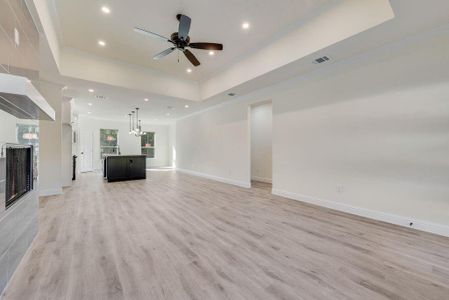 Unfurnished living room with ceiling fan with notable chandelier, a tray ceiling, and light wood-type flooring