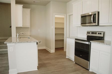 Kitchen featuring appliances with stainless steel finishes, kitchen peninsula, light stone countertops, and white cabinets