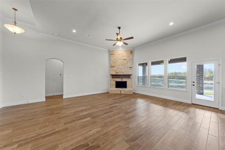 Unfurnished living room with a stone fireplace, ceiling fan, and ornamental molding