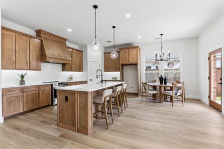 Kitchen with premium range hood, a kitchen island with sink, light hardwood / wood-style floors, and stainless steel electric range