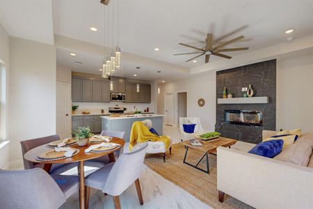 Dining room with a raised ceiling, light tile flooring, ceiling fan, and a fireplace