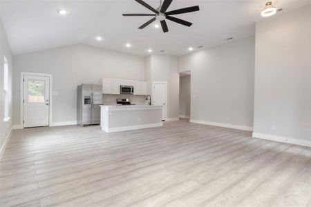 Unfurnished living room featuring high vaulted ceiling, ceiling fan, sink, and light hardwood / wood-style flooring