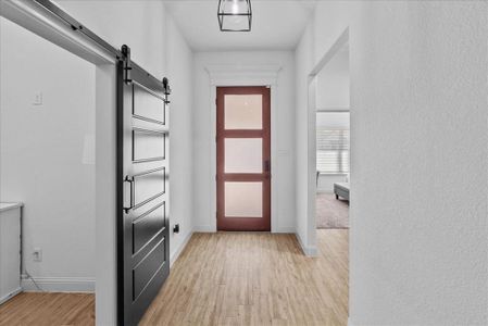 Doorway to outside featuring a barn door, light wood-style floors, and baseboards