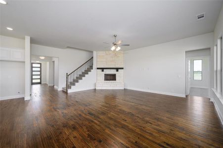 Unfurnished living room featuring ceiling fan, a stone fireplace, and dark wood-type flooring