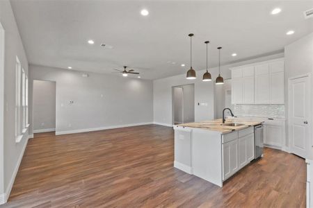 Kitchen featuring dark hardwood / wood-style flooring, ceiling fan, decorative light fixtures, a center island with sink, and white cabinets