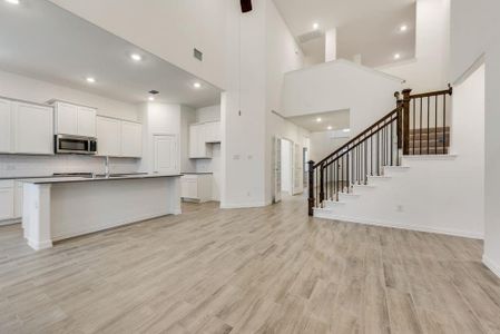 Kitchen featuring an island with sink, a towering ceiling, white cabinetry, and light wood-type flooring