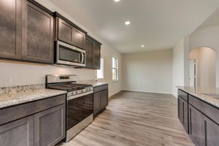 Kitchen with dark brown cabinets, light wood-type flooring, light stone counters, and appliances with stainless steel finishes