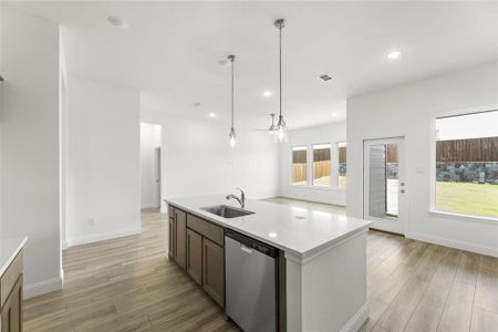 Kitchen featuring a wealth of natural light, hanging light fixtures, a center island with sink, stainless steel dishwasher, and sink