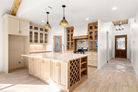 Kitchen featuring gas stove, beam ceiling, sink, an island with sink, and custom exhaust hood