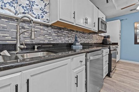 Kitchen featuring dark stone countertops, decorative backsplash, light wood-type flooring, stainless steel appliances, and white cabinets