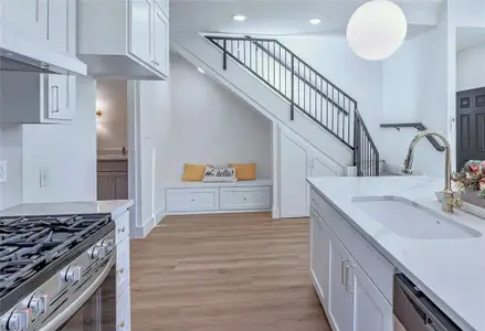 Kitchen featuring light wood finished floors, white cabinetry, a sink, dishwasher, and under cabinet range hood