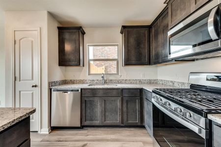 Kitchen with appliances with stainless steel finishes, light stone countertops, sink, light hardwood / wood-style flooring, and dark brown cabinetry