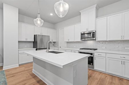 Kitchen featuring decorative backsplash, light hardwood / wood-style flooring, white cabinetry, and stainless steel appliances