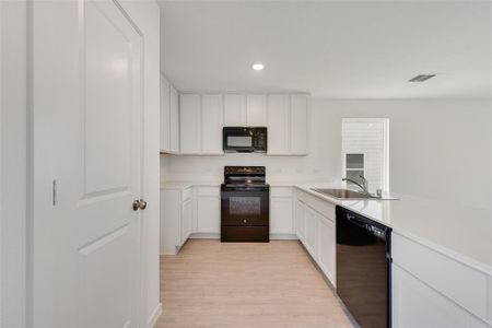 Kitchen featuring sink, white cabinetry, light wood-type flooring, kitchen peninsula, and black appliances