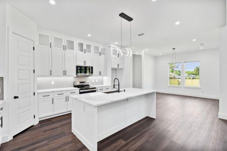 Kitchen featuring stainless steel appliances, hanging light fixtures, an island with sink, and white cabinets